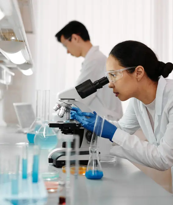 A woman looking through a microscope at some liquid.